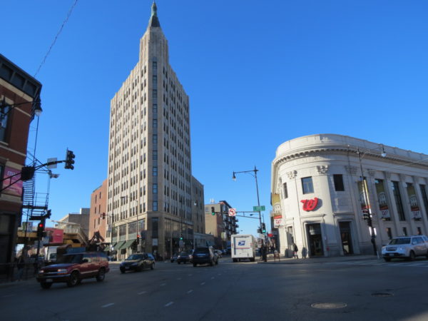 A three street intersection with white terra cotta corner Walgreens and an Art Deco 12 story corner tower.