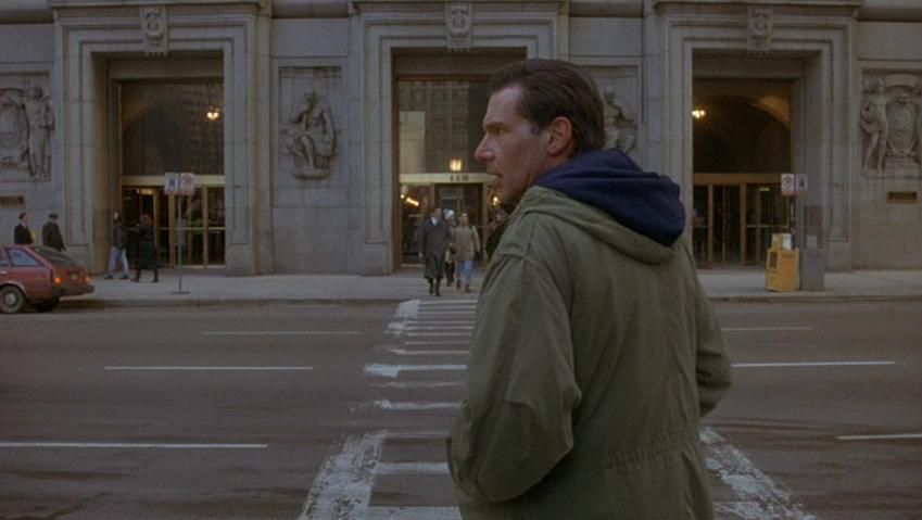 A movie still from The Fugitive of Harrison Ford as Richard Kimble walking towards a building with dinstince bas reliefs at the entrance