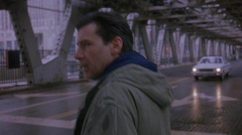 A Fugitive movie still of Harrison Ford as Richard Kimble crossing the street at a double-deck bridge. 