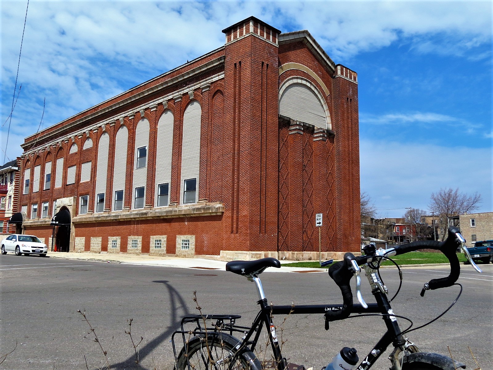 A tour bike standing in front of a long tall red brick vertical pile covered window former synagogue.