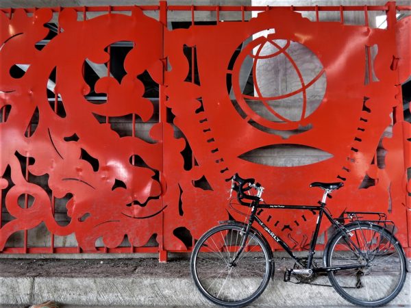 A tour bike leaning in front of a red metal sheet with punchouts including a globe.