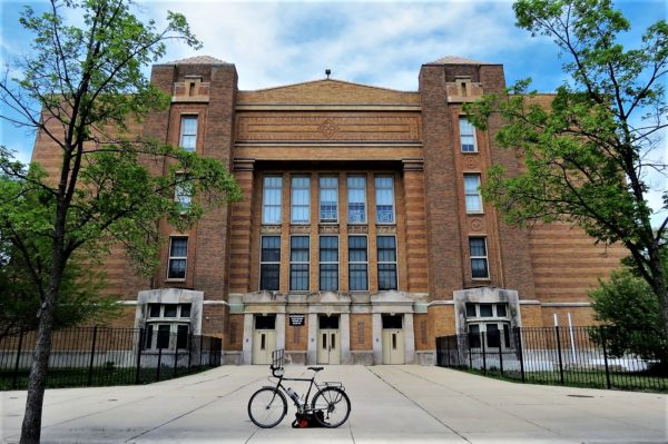 A tour bicycle standing in front of a tan brick solid mass Prairie style school building