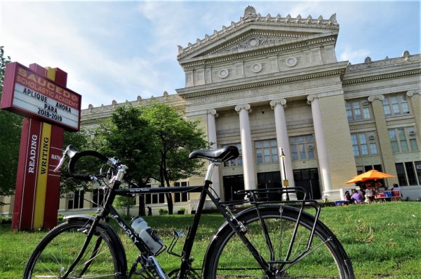 A tour bicycle standing in front of white Neo-Classical columned school entry.