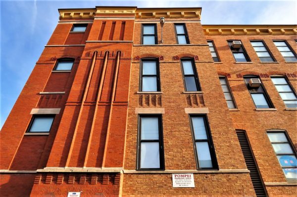 Looking up a four story red brick Italiante building with thin vertical windows and strong vertical brick lines