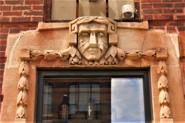 A limestone Art Deco face above a window framed by limestone garland