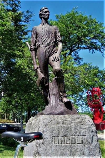 A tour bike seat in front of a bronxe sculpture of a young Abraham Lincoln with an ax in hand.