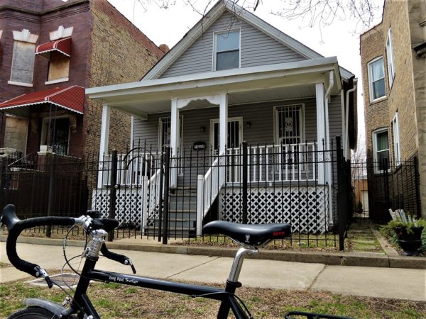 A tour bike in front of a one and half story wood frame with gray siding and white trim house