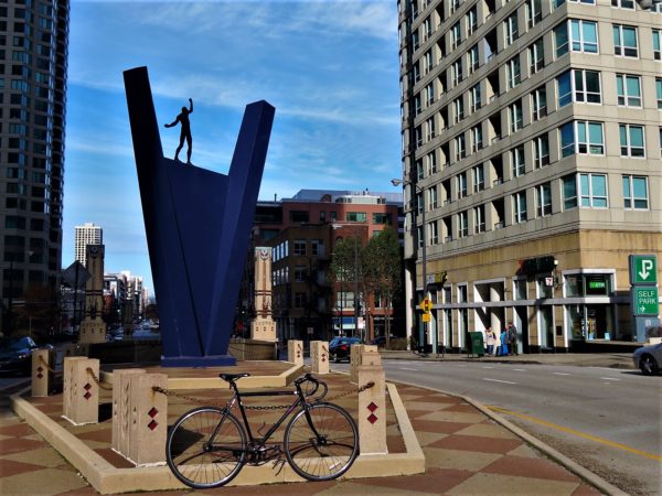 A tour bike standing in front of a blue triangular sculpture with a figure delicately walking across the top side
