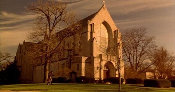 A movie still of a limestone Gothic Revival church in evening sun