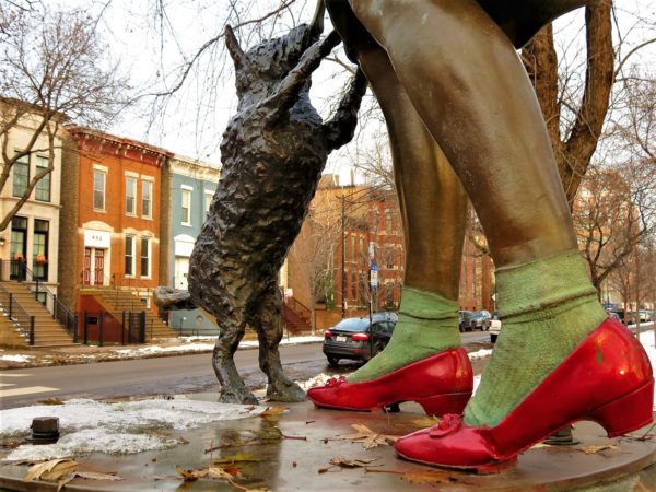 The bronze calves in red shoes and dog on hind legs of a statue with Italiante two and half stories in the background.