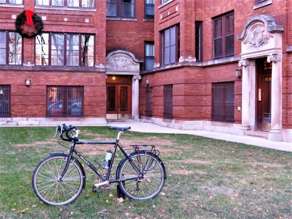 A tour bike standing in the grassy courtyard of a red brick apartment building with limestone entrances.