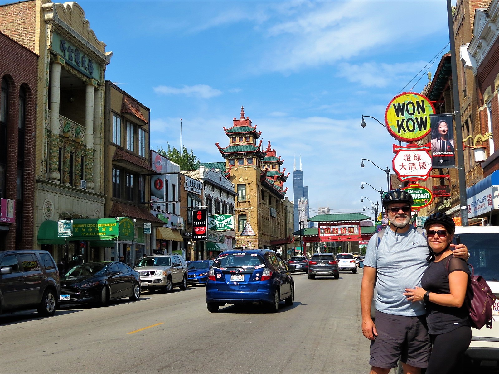 Two CBA bike tour riders posing in front of a road with Chinese style buildings with the Willis Tower skyscraper in the background.