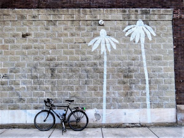 A tour bike leaning on a thick rough stone gray brick wall with two white painted palm trees.