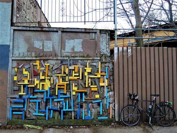 A tour bike leaning on a brown painted fence next to a yellow and blue painted wood block wall arrangement.