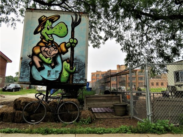 A tour bike standing under a transport trailer with a T Money De Larue smiling farmer lizard at City Farm.