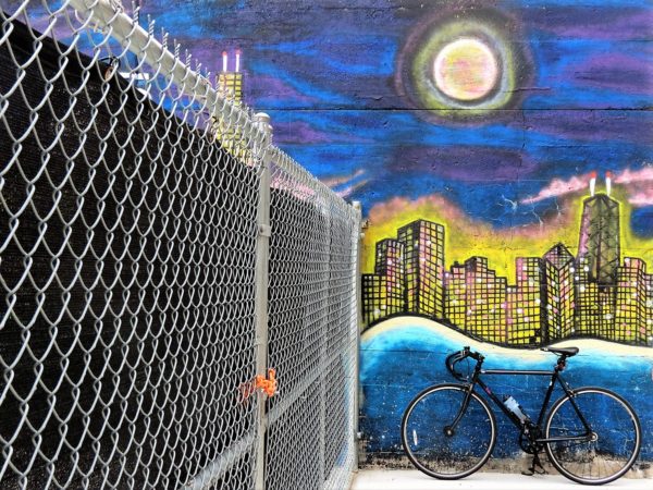 A tour bike leaning on a mural of a glowing Chicago skyline under the moon.