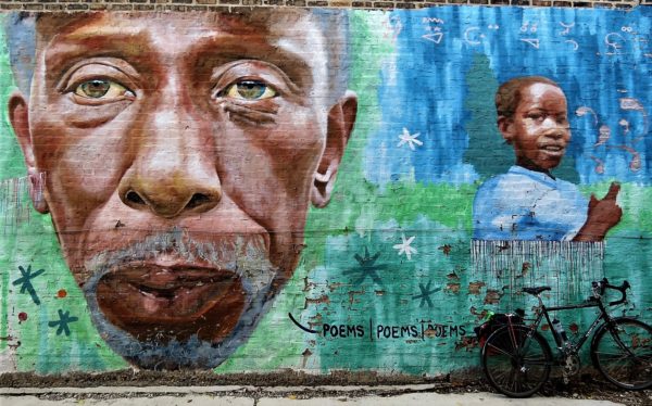 A tour bike leaning on a blue green Jeff Zimmerman mural of a bearded older black man and child.