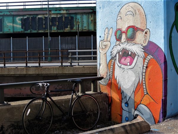 A tour bike next to a Jake Merten mural of a bald old man with a purple backpack and sunglasses.