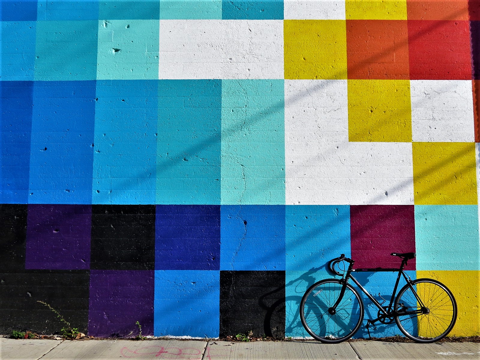 A tour bike leaning on a Felipe Pantone mural of multicolored squares.