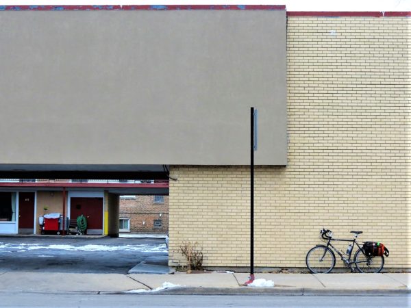 A tour bike leaning on a pale brown and yellow mid-century motel wall.