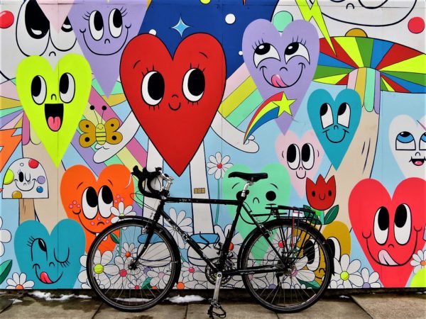 Tour bike leaning on a smiling hearts mural.