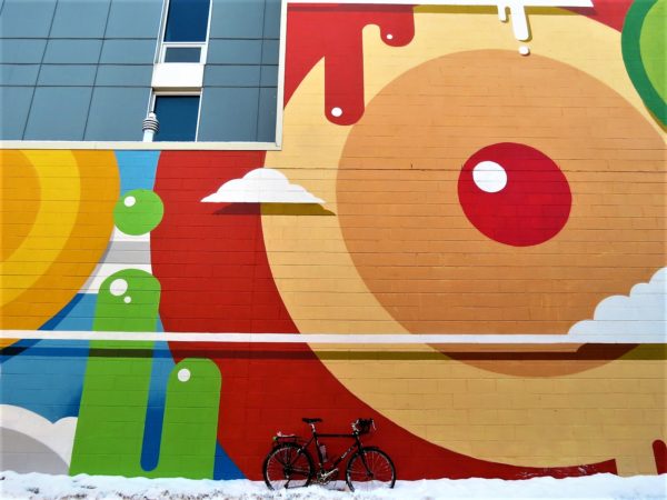 Primary colored paint drip style mural with tour bike in snow in front.