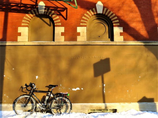 Tour bike leaning on red brick brown painted wall with yellow brick accented covered up windows.