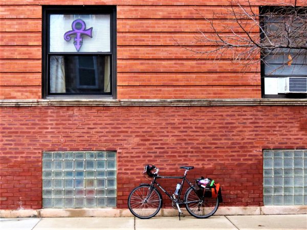 Bicycle leaning on a brick wall with a Prince symbol in the window.