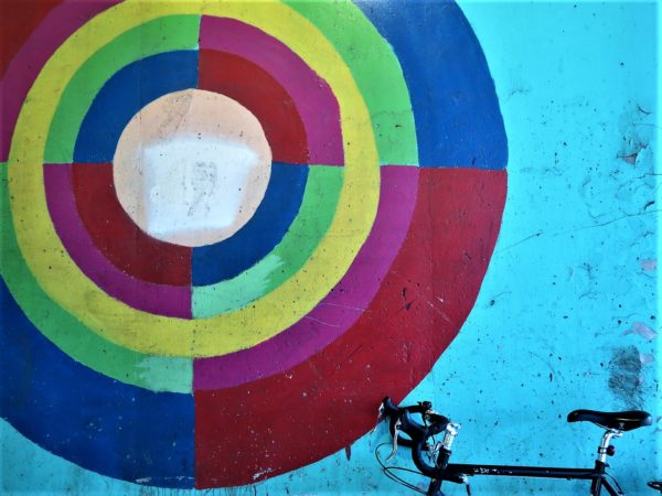 Multi-colored circle painted on light blue wall with a bike during a tour ride.