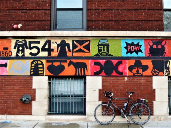 Bicycle underneath a colorful points of history on school exterior.