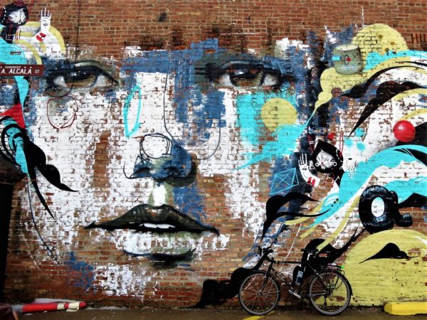 A tour bike leaning on a mural of a face and yellow and aqua waves.