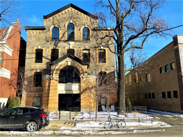 A tour bike in front of the yellow brick large arched entrance former Sisters of the Resurrection Convent turned condos.