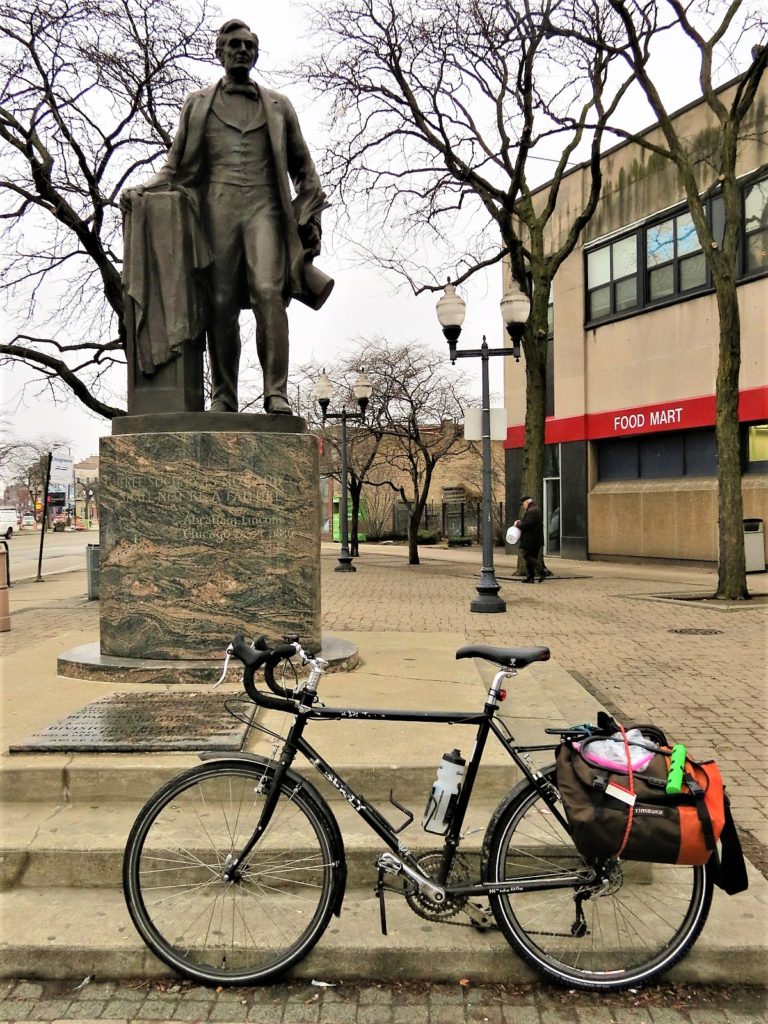 US President standing with hat in hand and a bike during a tour ride.