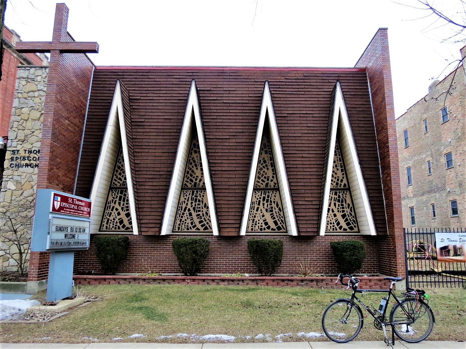 A tour bike standing in front of one side of the mid century modern steep roofed triangle windowed St. Thomas Episcopal Church.
