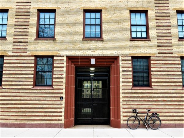 A tour bike leaning next to the red terra cotta entrance of yellow and red brick patterned Rosenwald Apartments.