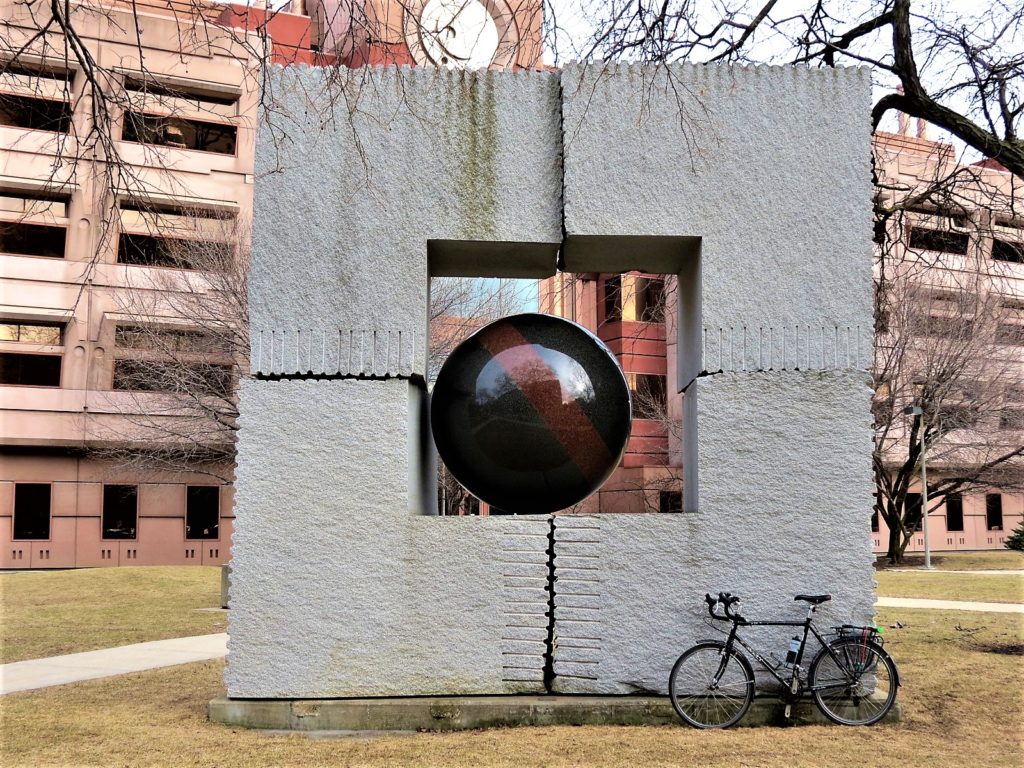 Four part stone sculpute with granite ball in the middle with a bike during a tour ride.