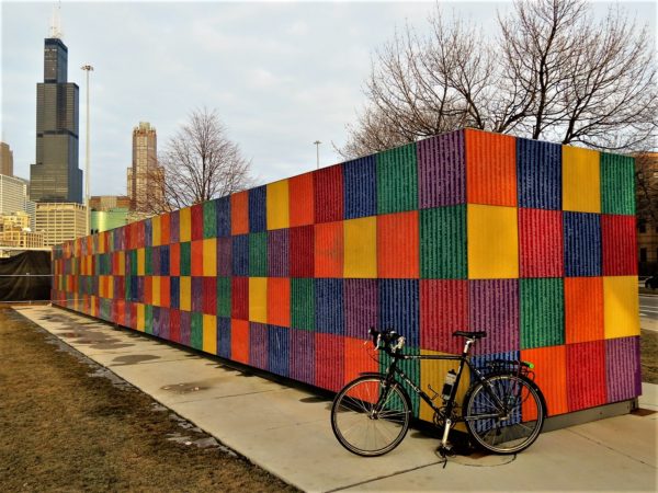 A tour bike leaning on Tony Tasset's multi color square covered rectangular box sculpture Artists Monument with the