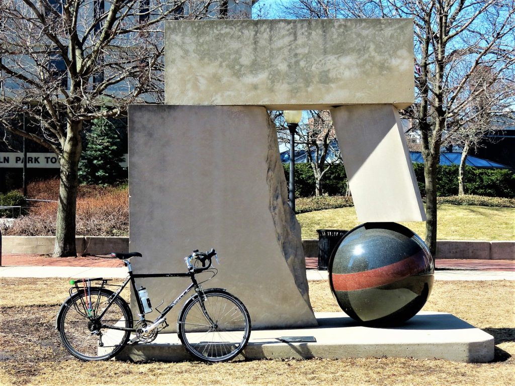 Stone sculpture leaning on granite ball with a bike during a tour ride.