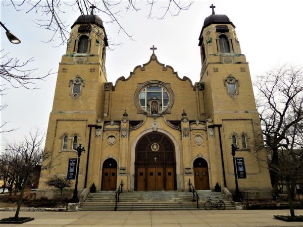 A tour bicycle in front of the yellow brick two towered Baroque Our Lady of Lourdes church.