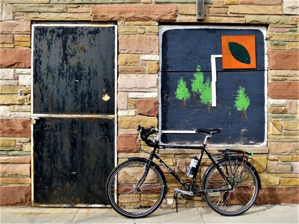 A tour bike leaning on a multicolored stone wall with a nature themed wooden collage.