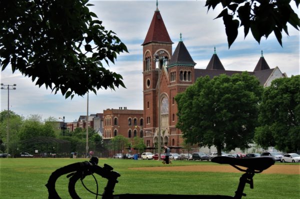 Silhouette of a tour bike in front of red brick Romanesque St. Boniface church between trees.