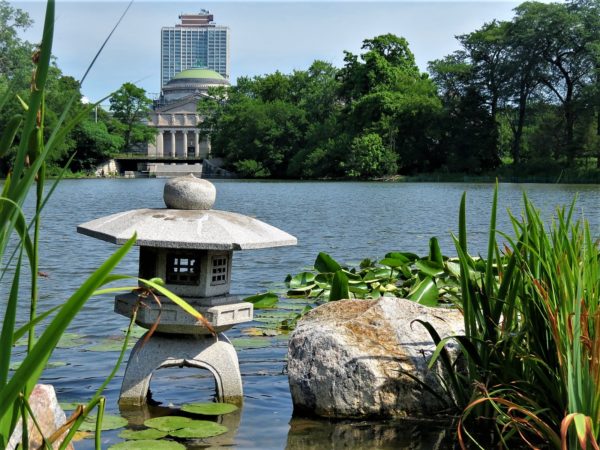 A Japanese stone lantern standing in the Jackson Park Lagoon with the neoclassical Museum of Science and Industry in the background.