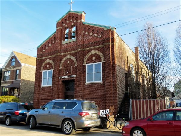 A tour bike parallel parked with cars in front of a red brick church