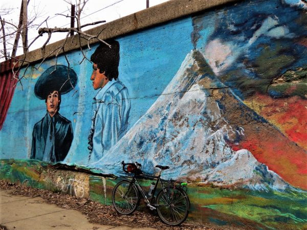 Two men and a mountain mural with a leaning tour bicycle.
