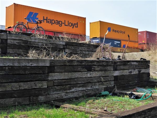 A tour bike standing in an urban garden next shipping to containers on the railroad 