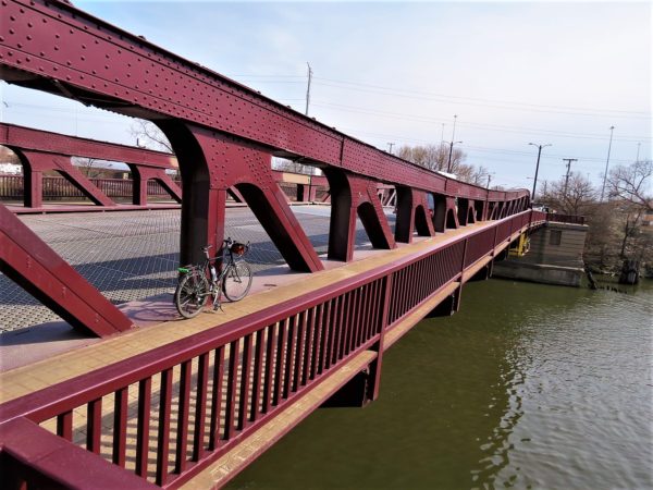 A tour bike leaning on a painted maroon movable bridge with the river below.