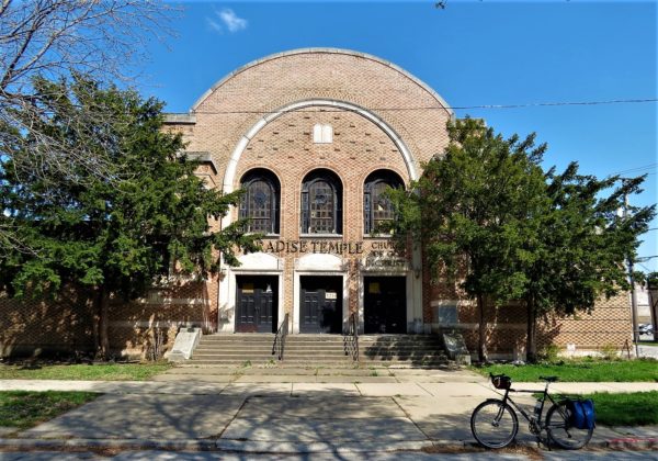 Rounded former synagogue facade between two trees with a tour bike in front.