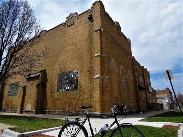 A fortress like yellow brick former synagogue now church with a tour bike in front.