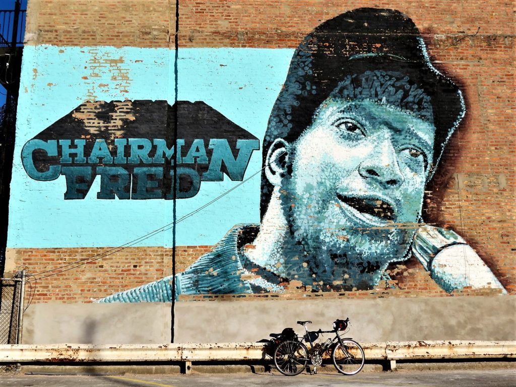 A tour bike leaning on a mural of Fred Hampton speaking into a microphone with the words Chairman Fred