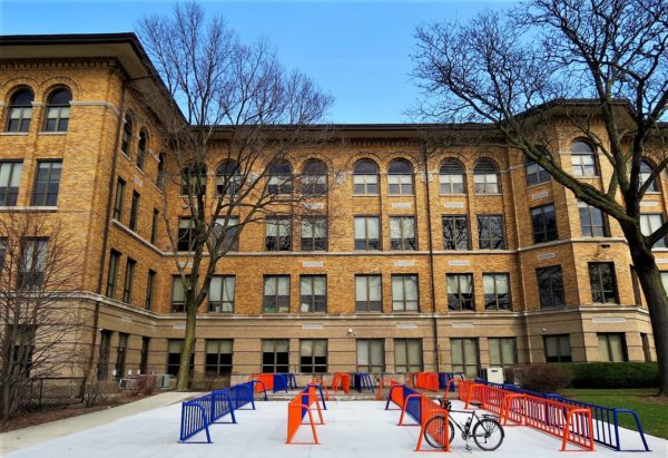 Yellow brick Italianate school building with one tour bike in the bike racks in front